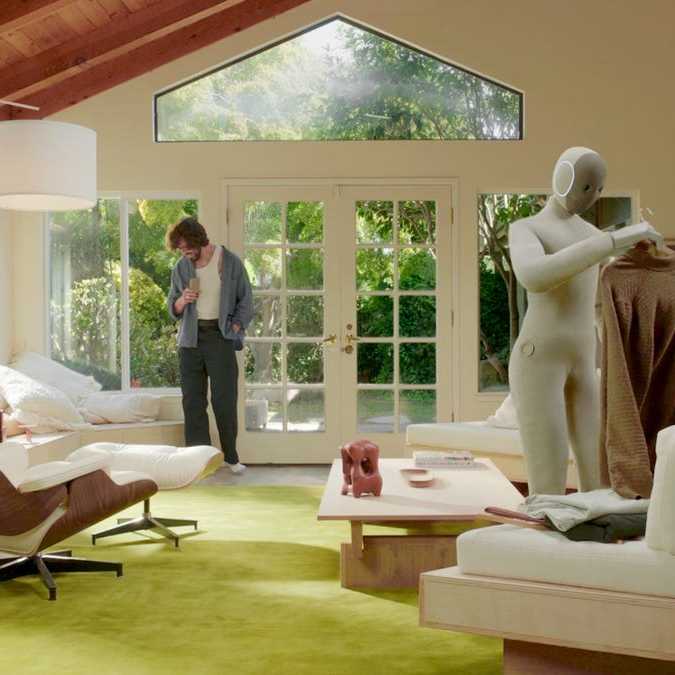 A humanoid robot folds laundry in an upscale living room.