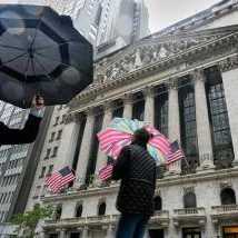 People with umbrellas pass the New York Stock Exchange, Monday, Oct. 13, 2025. (AP Photo/Richard Drew)