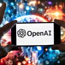 The OpenAI logo on a cell phone in front of an image on a computer screen generated by ChatGPT's Dall-E text-to-image model.