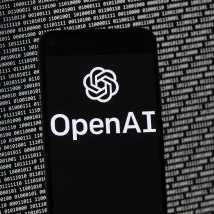 The OpenAI logo appears on a mobile phone in front of a computer screen with random binary data, Thursday, March 9, 2023, in Boston. (AP Photo/Michael Dwyer)